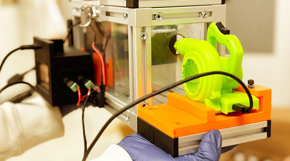 A machine to detect certain molecules in air samples. The machine consists of a glass box connected with various wires, with a green air pump on one side.