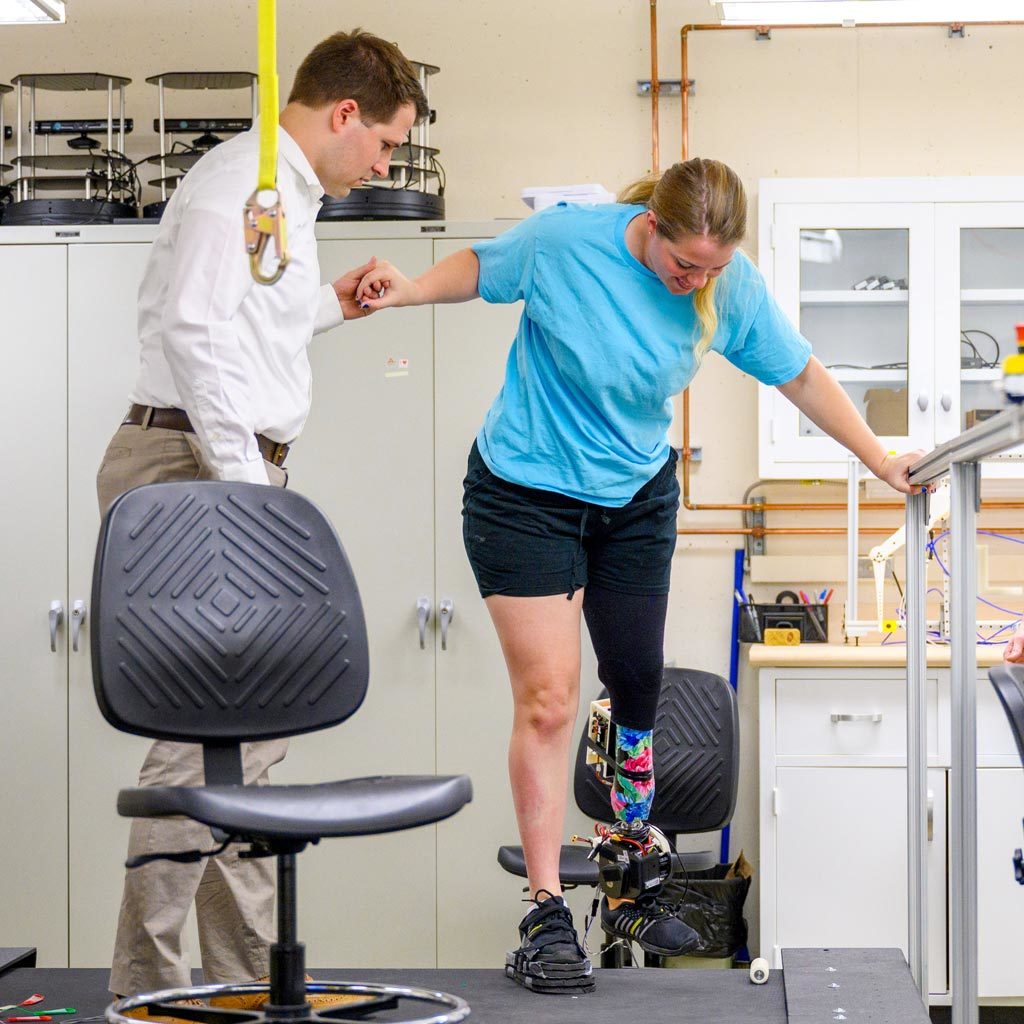 Patrick Wensing, director of the Robotics, Optimization, and Assistive Mobility (ROAM) Lab, helps Laura Light onto the treadmill to test a powered prosthesis in Fitzpatrick Hall of Engineering.
