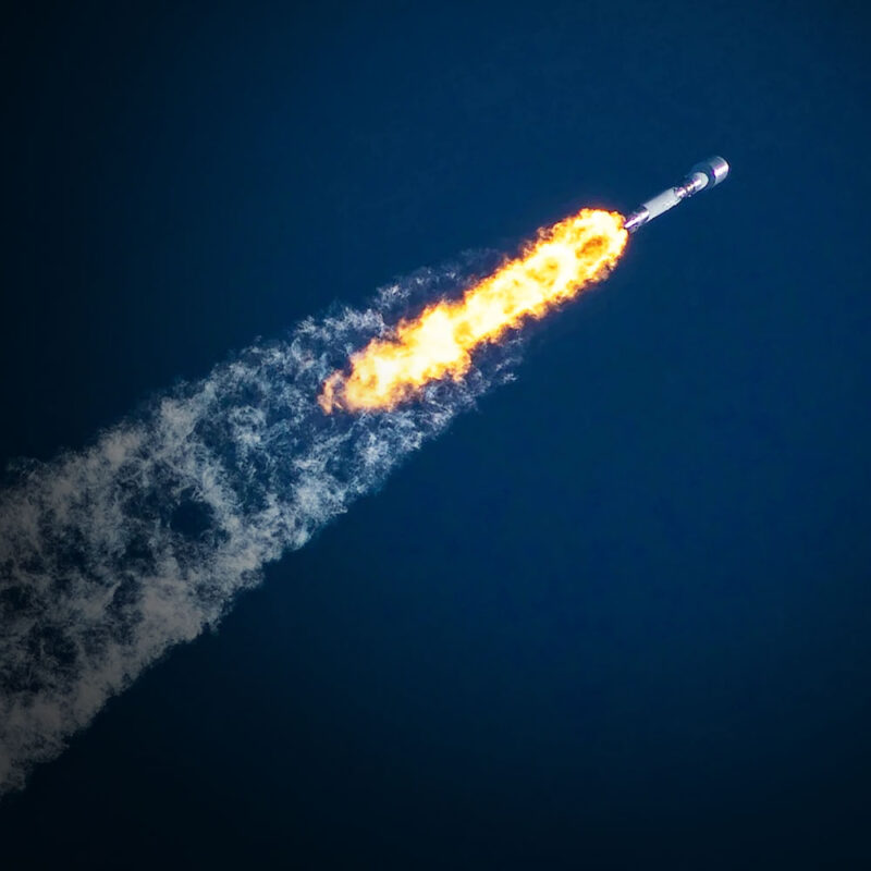 A rocket takes off from a launch pad, surrounded by billowing smoke and flames.
